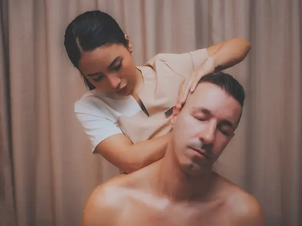 Thai massage therapist massaging a seated man in a curtained treatment room