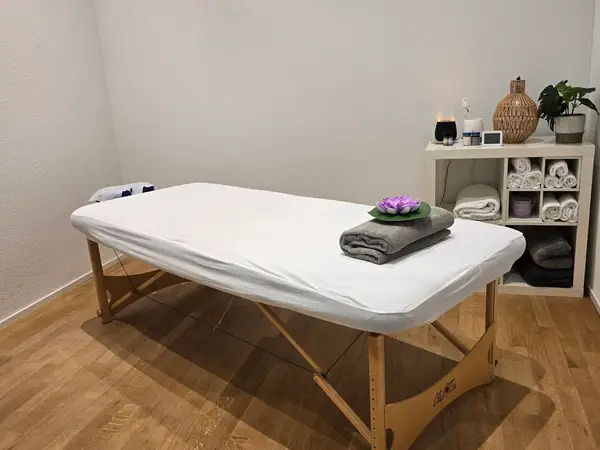 Minimal massage room with a white table, folded towels, and shelving