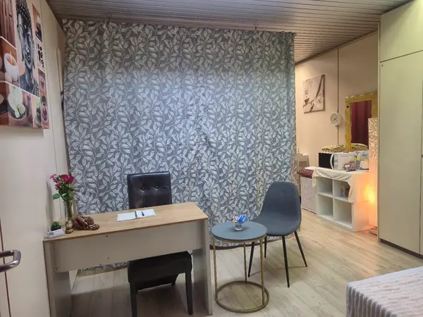 Small massage reception room with desk, chairs, patterned wallpaper, and warm lighting
