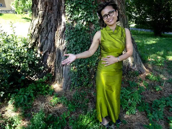 Woman in green dress standing by a large tree outdoors