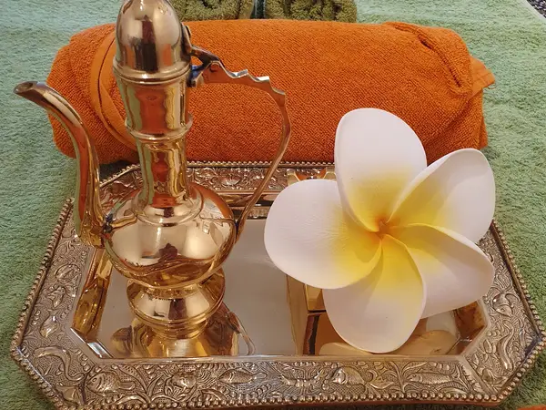 Decorative tray with brass teapot, white flower, and orange towel on green fabric