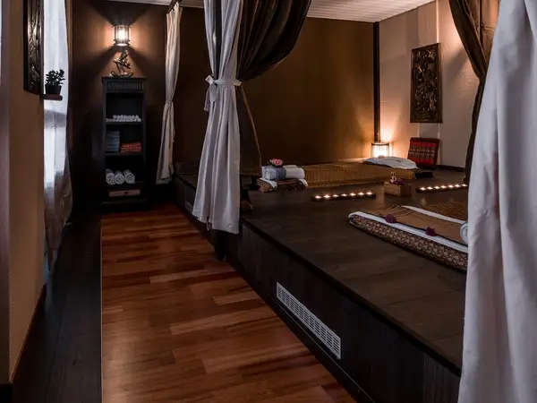 Dim Thai massage room with raised mats, curtains, candles, and warm wood decor