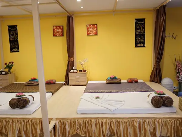 Thai massage room with mats, folded towels, brown curtains, and yellow walls