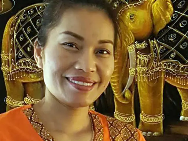 Smiling woman in orange before ornate gold elephant tapestry