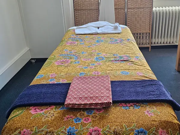 Massage table with floral cover, towels, and folded blanket in a quiet treatment room