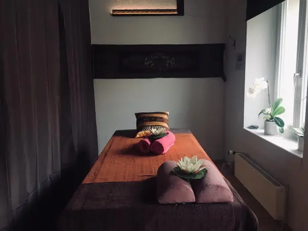 Dim Thai massage room with a treatment bed, cushions, and window orchids