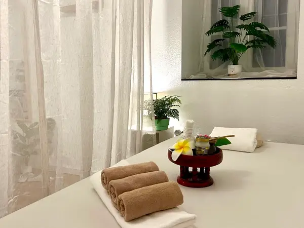 Bright massage room with treatment bed, folded towels, and sheer curtains