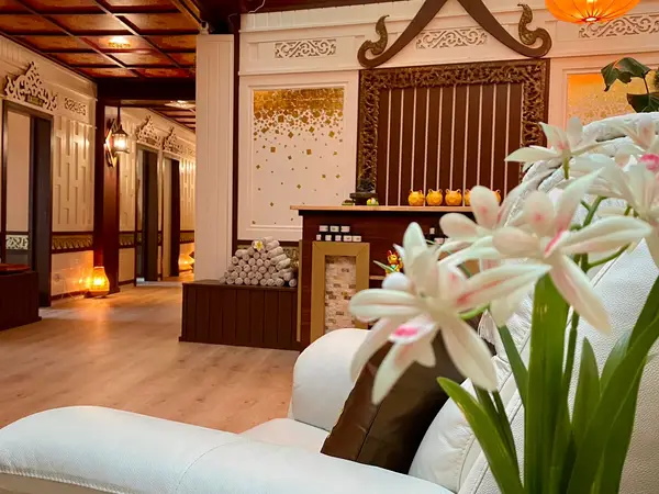 Warm Thai spa reception with carved decor, candles, and white flowers