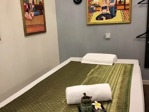 Massage room with Thai artwork, neatly made bed, and folded towels