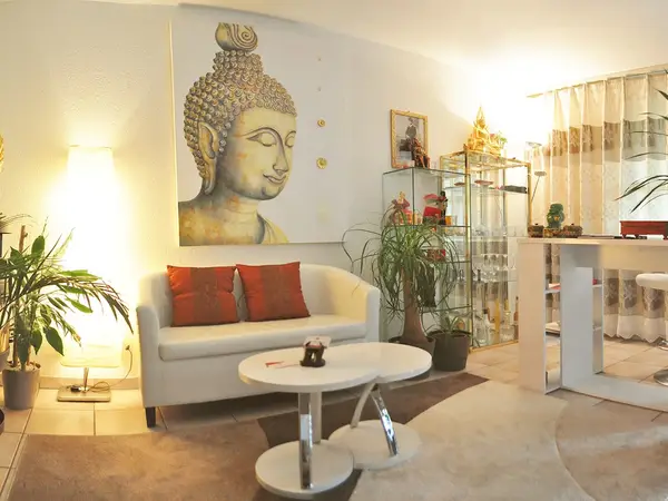 Bright Thai massage reception with Buddha artwork, sofa, plants, and glass display cabinet