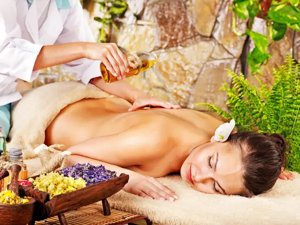 Thai massage scene with woman receiving oil massage on a padded table, surrounded by flowers and plants