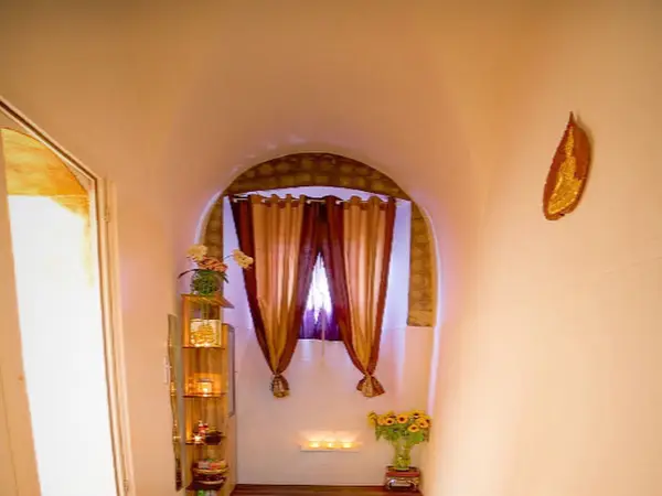 Warmly lit massage room with arched window, curtains, candles, and floral decor