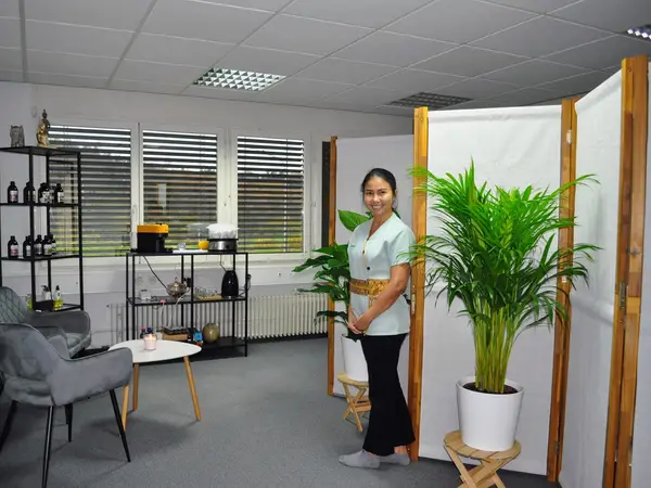 Bright Thai massage room with plants, seating, shelves, and a smiling woman