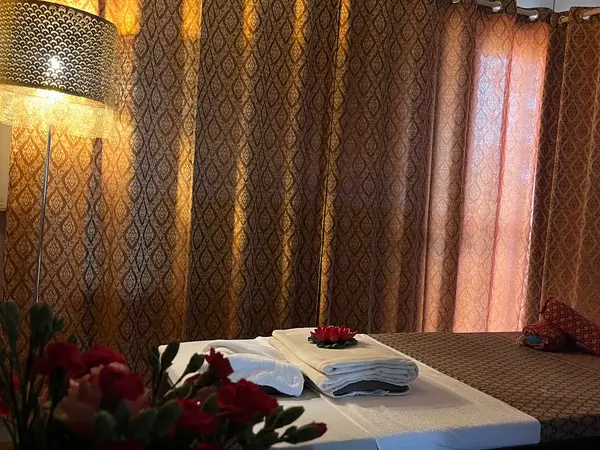 Warm Thai massage room with patterned curtains, lamp, and neatly made massage bed