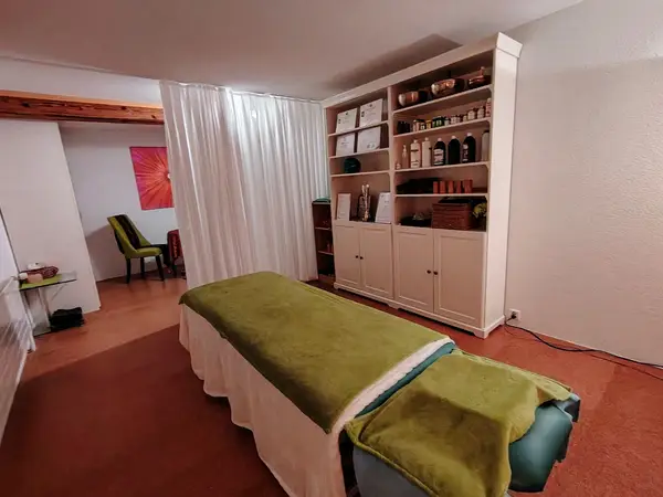Massage room with green table, white curtains, and shelving of products
