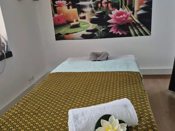 A small massage room with a bed, lotus wall art, and calm decor