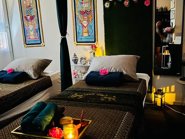 Dim Thai massage room with two treatment beds, candles, and wall art