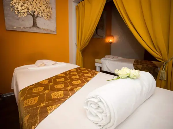 Warm massage room with two treatment beds, yellow curtains, and soft lighting