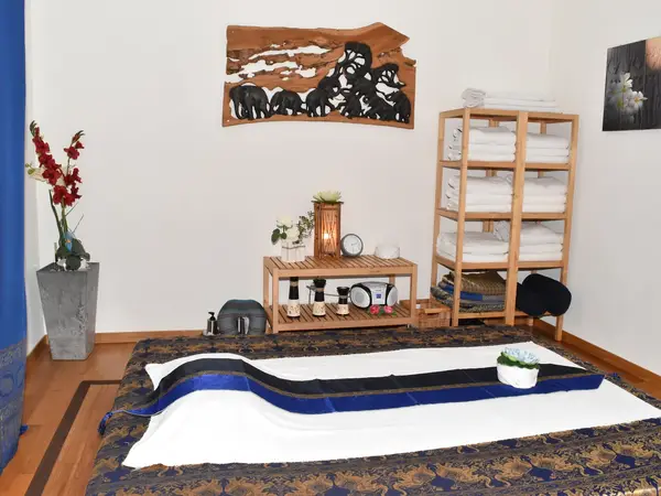 Thai massage room with low mat, shelves of towels, and soft decor